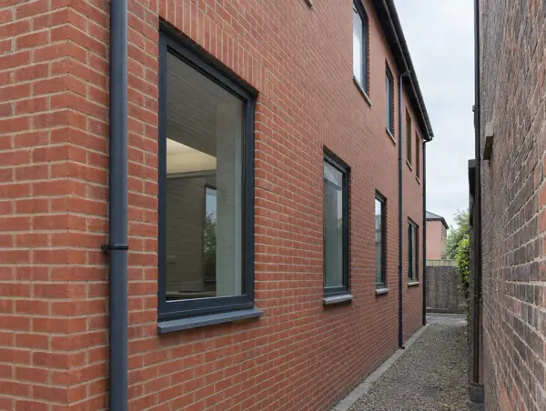 Brick side elevation close to a neighbouring wall with fixed dark-framed windows